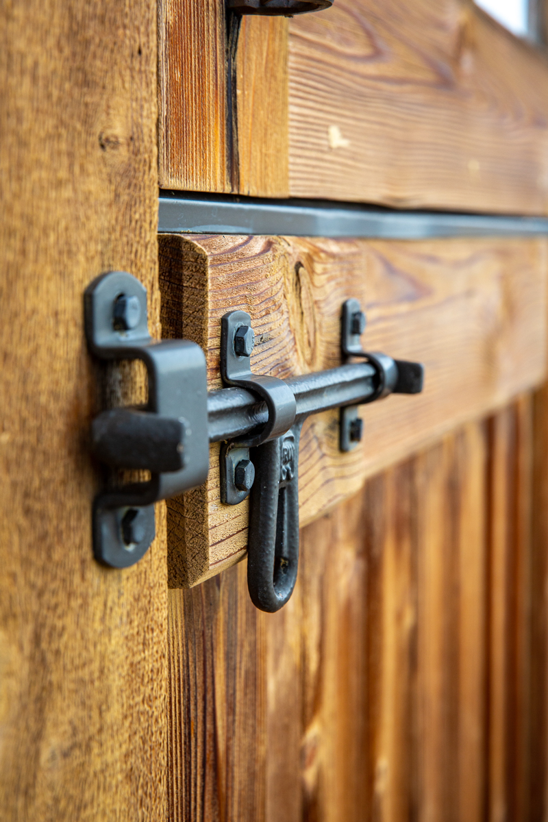 A close-up of a metal latch lock on a wooden door, showing the texture of the wood and the details of the black metal locking mechanism.