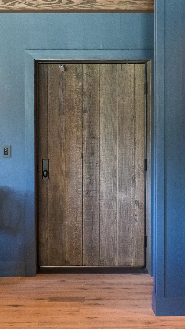 A rustic wooden door with vertical planks set in a frame within blue-painted walls and a light wooden floor.