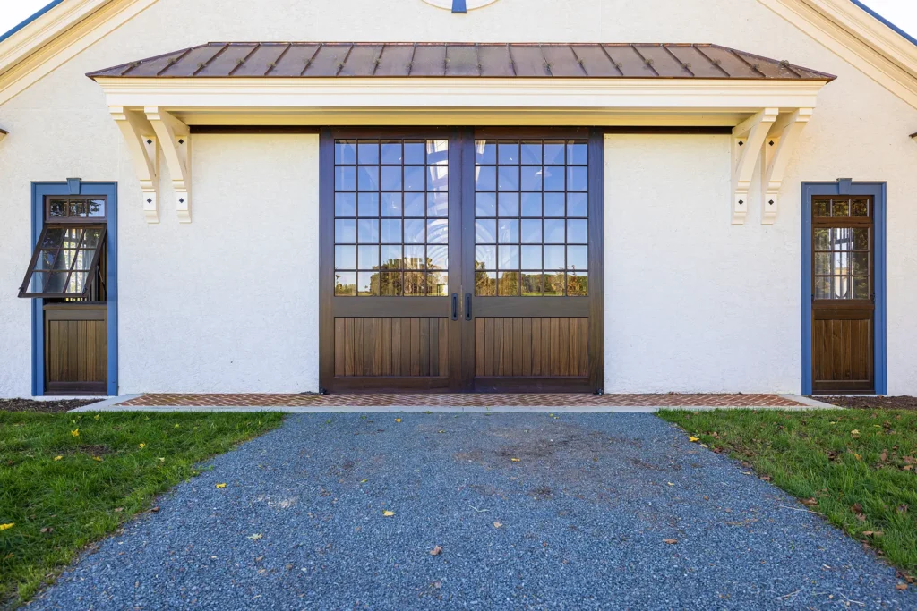A building with large double glass doors and two adjacent windows on each side, one window partially open. The entrance area is paved with gravel and bordered by green grass.