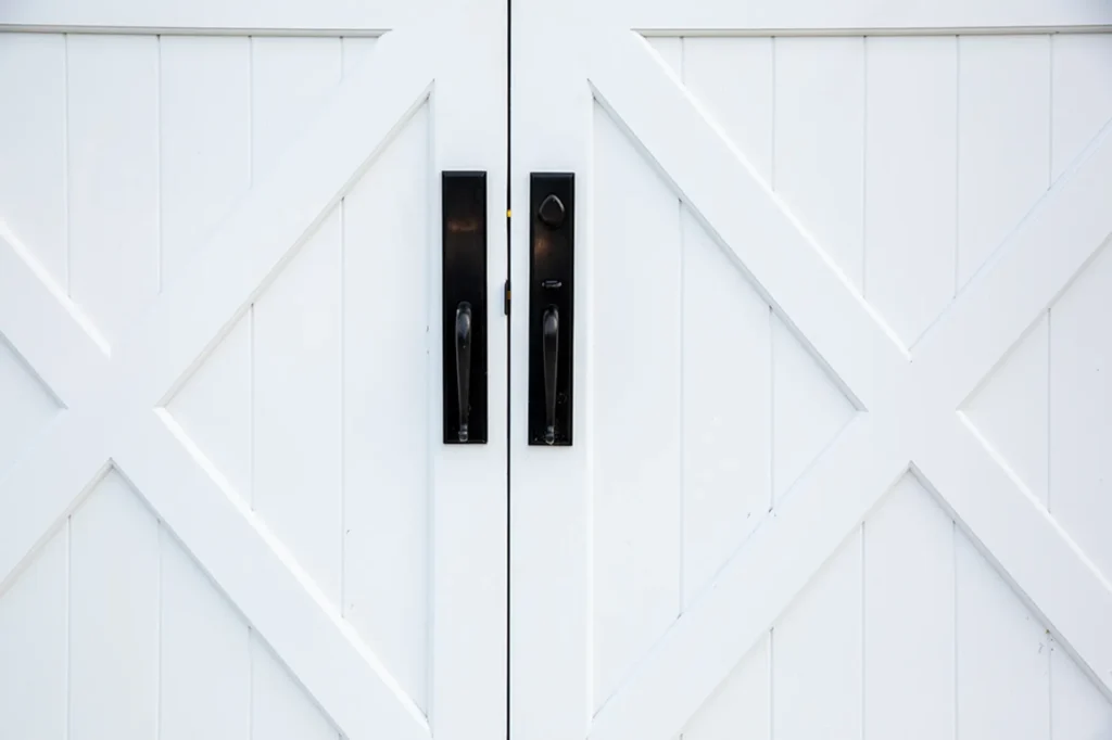 Close-up of white double doors with black handles, featuring a diagonal and vertical panel design in a crisscross X pattern.